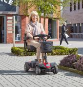 Lady happily driving a mobility scooter on pavement in-between shops